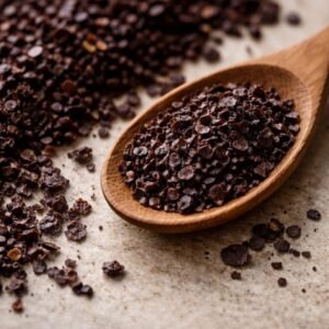 Dark Urfa pepper flakes on a stone surface with wooden spoon showing minimal seeds and oily texture