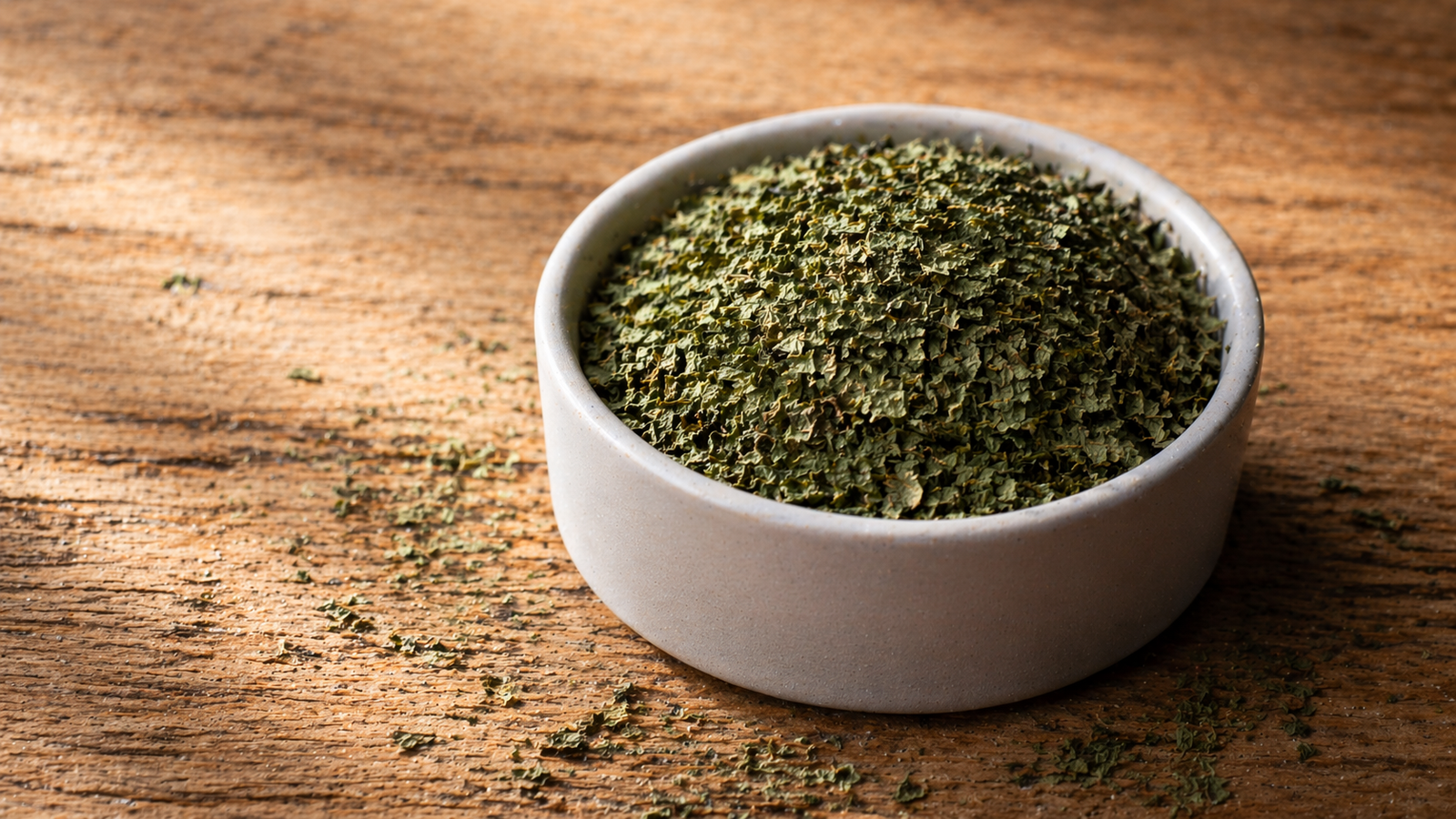 Dried mint flakes mounded in a small white ceramic ramekin on a wooden surface