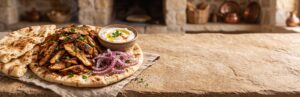 Chicken shawarma on warm pita with sumac-dusted red onion and a bowl of garlic sauce
